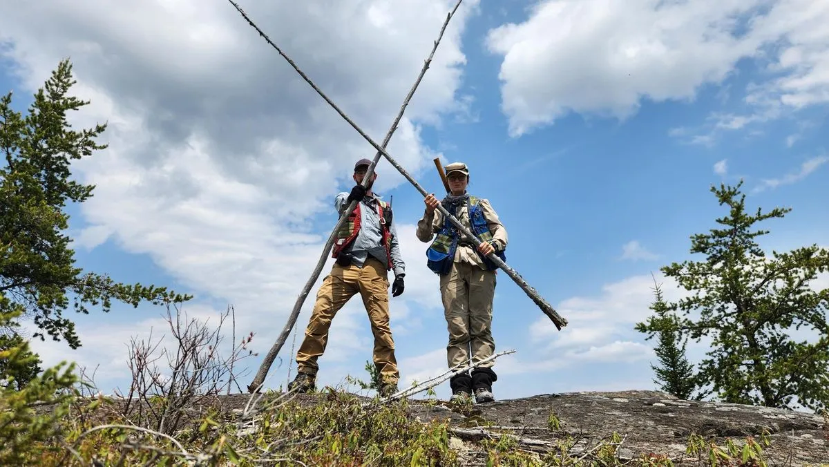 Two geologists carrying rods across a pegmatite outcrop