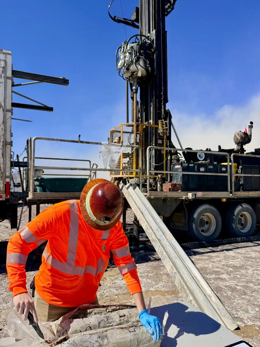Technician sampling sonic drill core beside the rig